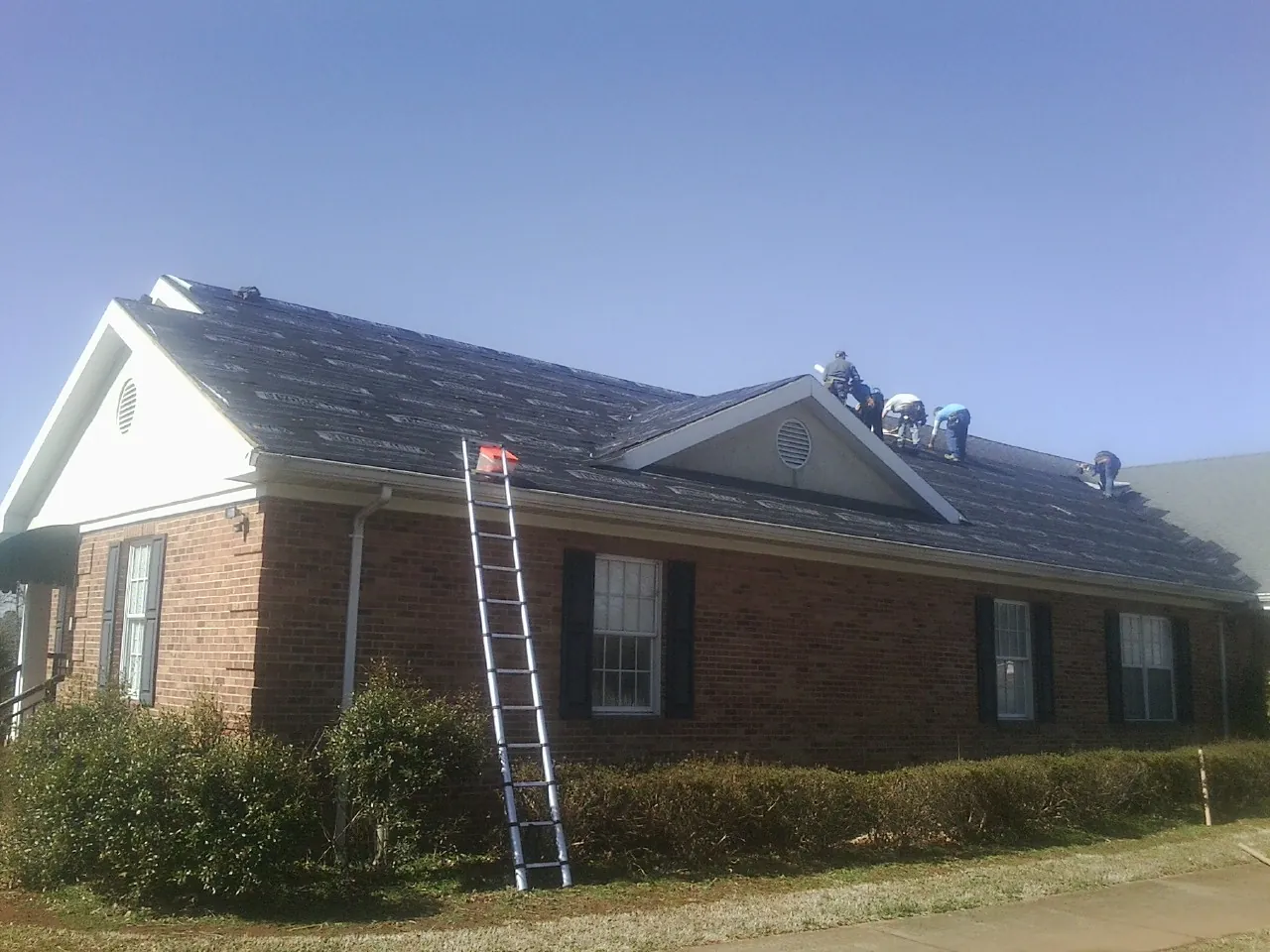 Crew tearing shingles off a brick ranch roof with a ladder set — Emergency Roof Repair work by our crew in Chatom