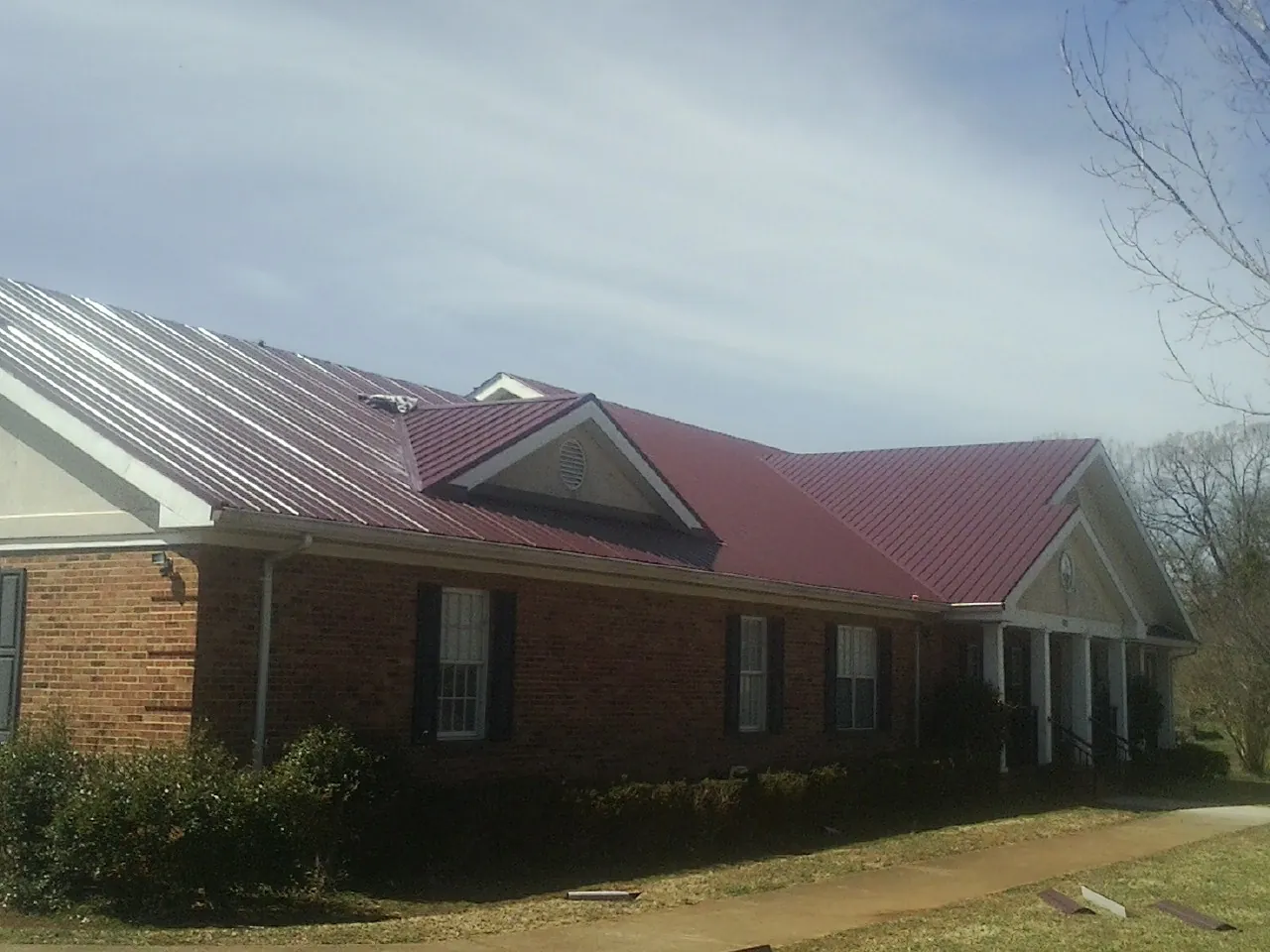 Red metal roof with gabled entries on a long brick building, from a Hail Damage Roof Repair job in Chatom