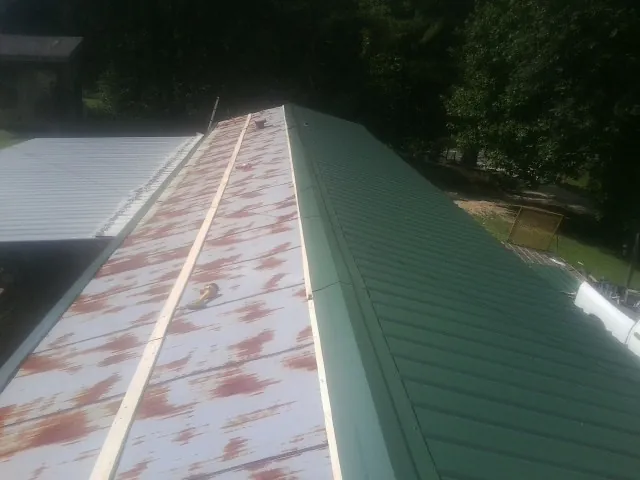Old rusted panels beside newly installed green metal roofing — Wind Damage Roof Repair by Roofing Brothers in Chatom