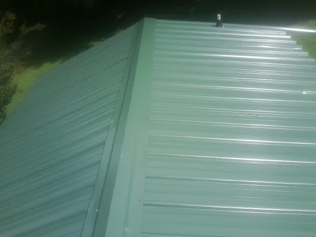 New green metal panels meeting at the ridge of a roof — Flat Roof Repair work by our crew in Chatom