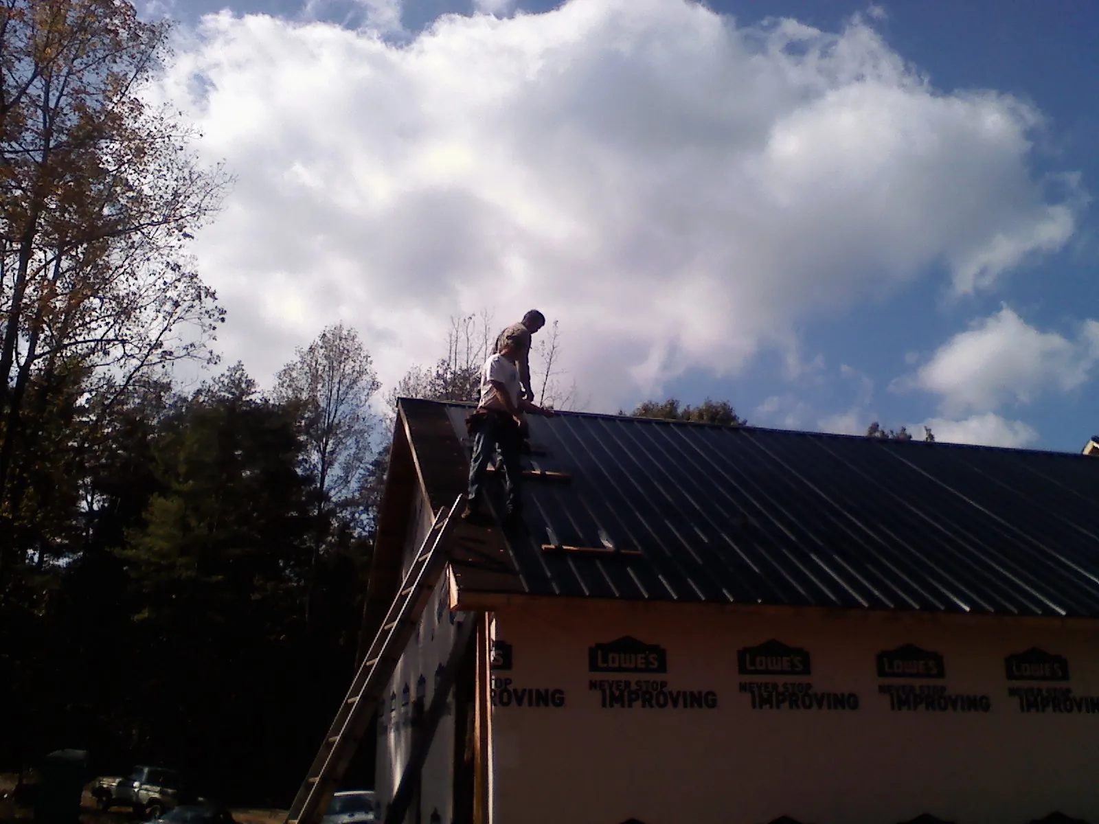 Roofer fastening dark metal panels high against a cloudy sky, from a Roof Inspection job in Chatom